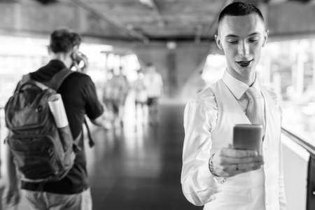 Happy young handsome androgynous businessman using phone in the cityの写真素材