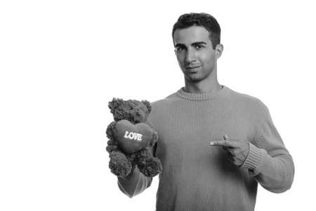 Young handsome Iranian man holding teddy bear with heart and love sign while pointing finger ready for Valentines dayの写真素材
