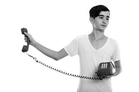 Studio shot of young stressed Persian teenage boy holding old telephone awayの写真素材