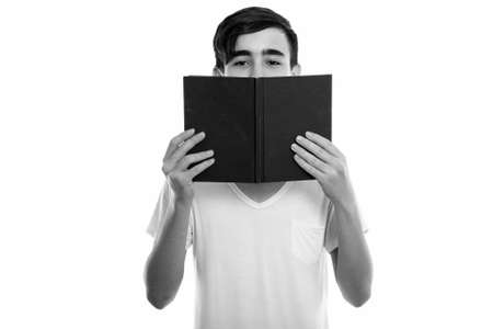 Studio shot of young handsome Persian teenage boy hiding behind bookの写真素材
