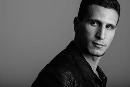 Studio shot of young muscular Persian man looking back while thinking ready for action against gray backgroundの写真素材