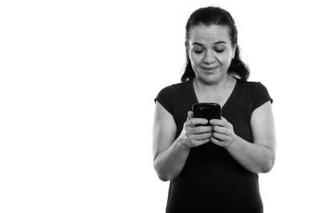 Studio shot of happy mature Persian woman smiling and laughing while using mobile phoneの写真素材