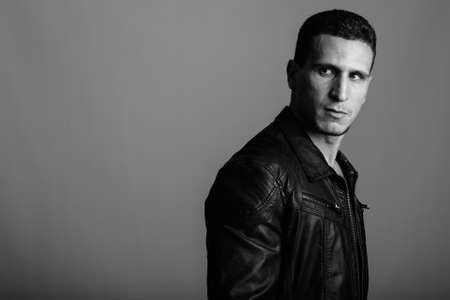 Studio shot of young muscular Persian man thinking while looking back against gray backgroundの写真素材