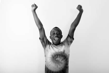 Studio shot of young happy black African man with both arms raised up against white backgroundの写真素材