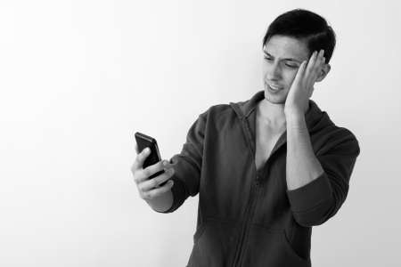 Studio shot of young handsome man having headache while using mobile phone against white backgroundの写真素材