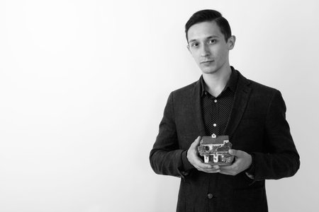 Studio shot of young handsome businessman holding house figurine against white background