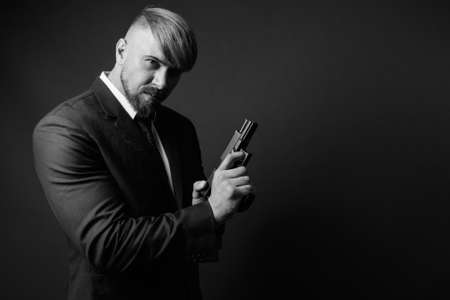 Bearded businessman with handgun against gray backgroundの写真素材