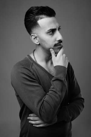 Young handsome Iranian man with mustache against gray backgroundの写真素材