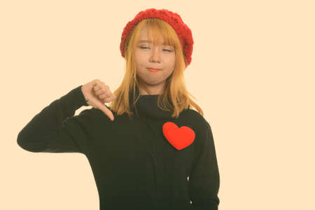 Young cute Asian woman giving thumb down with red heart on chestの写真素材