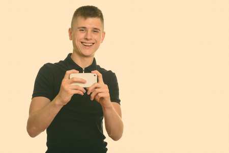 Young happy Caucasian man smiling and taking picture with mobile phone looking at camera