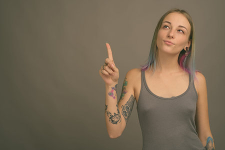 Young beautiful rebellious woman with multicolored hair against gray background