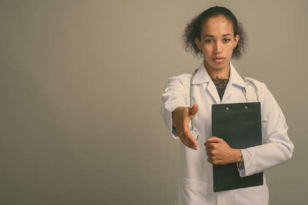 Young beautiful African woman doctor against gray backgroundの写真素材