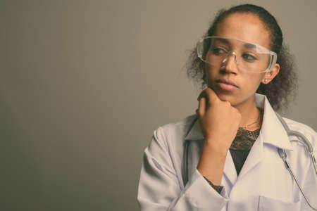 Young beautiful African woman doctor against gray backgroundの写真素材
