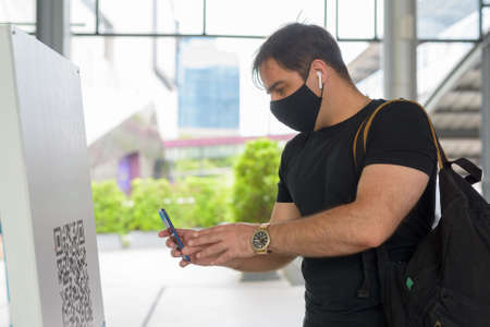 Portrait of Persian man with mask scanning QR code to register entryの写真素材