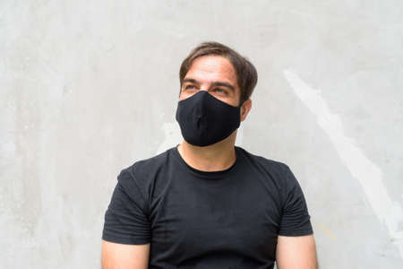 Portrait of Persian man with mask thinking against concrete wall outdoorsの写真素材