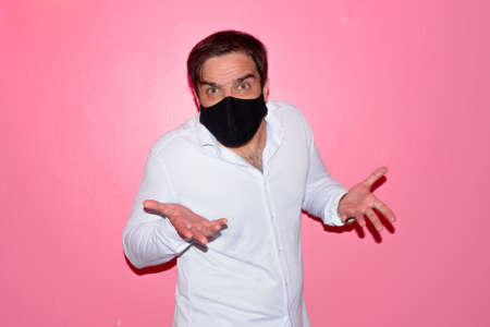 Stressed Persian businessman with mask shrugging shoulders against pink wallの写真素材