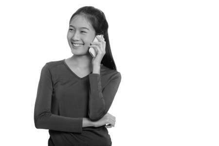 Young happy Asian teenage girl smiling and talking on mobile phone while thinkingの写真素材