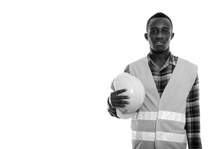 Studio shot of young happy black African man construction worker smiling while holding safety helmet