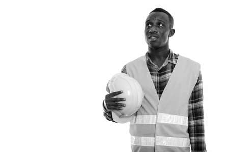 Studio shot of young black African man construction worker thinking while holding safety helmetの写真素材