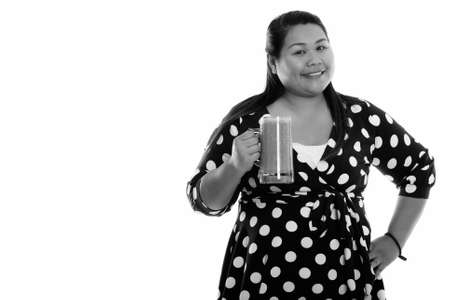 Studio shot of young happy fat Asian woman smiling while holding glass of vegetable smoothieの写真素材