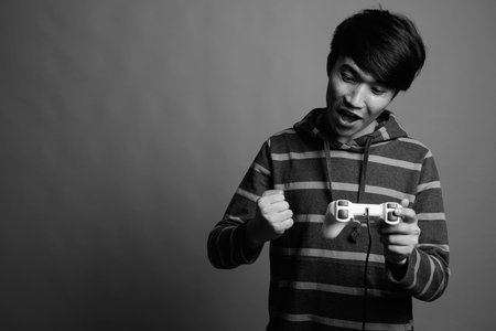 Young Asian man playing games against gray background
