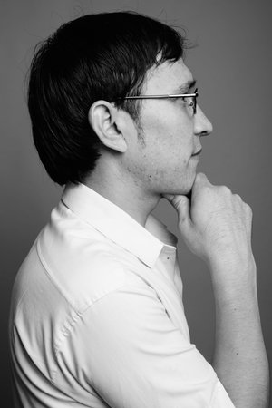 Young Asian nerd man wearing eyeglasses against gray background