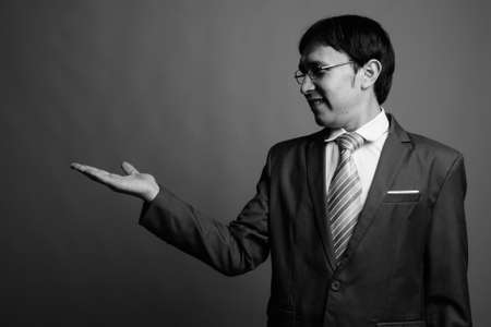 Young Asian businessman in suit against gray backgroundの写真素材