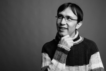 Young Asian nerd man wearing turtleneck sweater against gray backgroundの写真素材