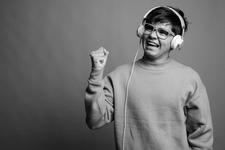 Young Asian teenage boy listening to music against gray background