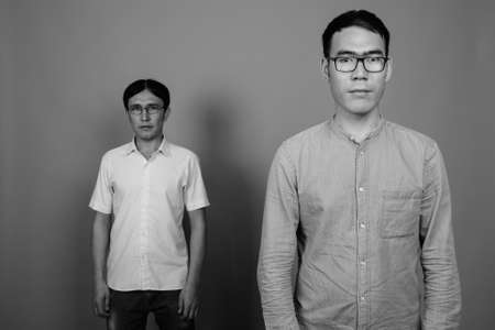 Two young Asian businessmen wearing eyeglasses together against gray backgroundの写真素材