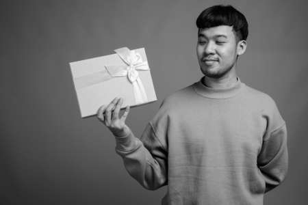 Portrait of young Asian man against gray backgroundの写真素材