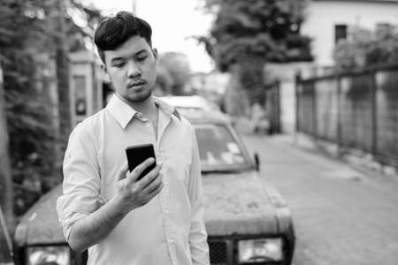 Young Asian businessman using mobile phone against rusty old carの写真素材