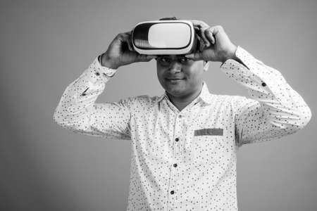 Young Indian businessman using virtual reality headset against gray backgroundの写真素材