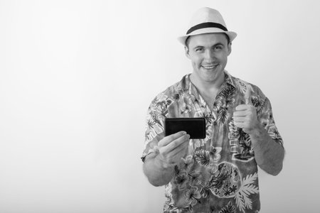 Studio shot of young happy muscular tourist man smiling while taking picture with mobile phone and...