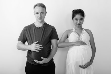 Young multi ethnic married couple holding tummies together against white backgroundの写真素材