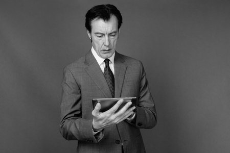 Mature handsome businessman in suit against gray background