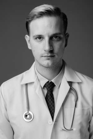 Young handsome man doctor with blond hair against gray backgroundの写真素材