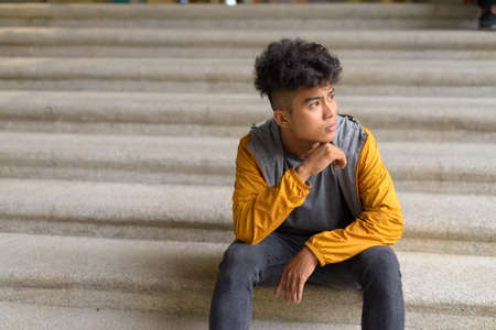 Young Asian man with curly hair thinking and sitting on staircase in the cityの写真素材