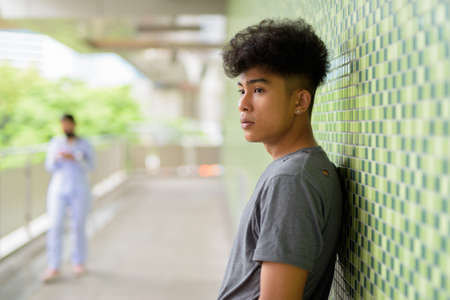 Profile view of young Asian man with curly hair at footbridge in the cityの写真素材