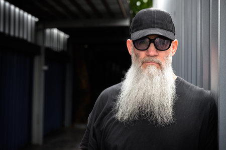 Mature handsome bearded hipster man with cap and sunglasses in the streets outdoors