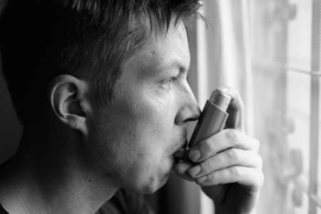 Portrait of stressed young man using asthma inhaler at homeの写真素材