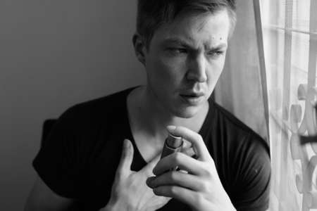 Portrait of stressed young man using asthma inhaler at homeの写真素材