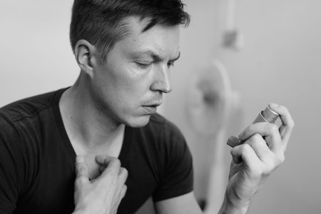 Portrait of stressed young man using asthma inhaler at home