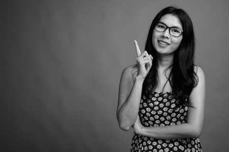 Portrait of happy Asian woman with eyeglasses against gray backgroundの写真素材