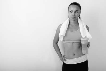 Studio shot of young Asian woman thinking while holding water bottle ready for gymの写真素材