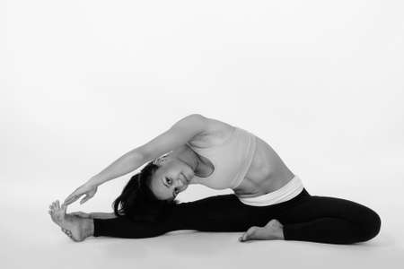 Full body shot of young Asian woman stretching to the side while reaching her feet against white backgroundの写真素材