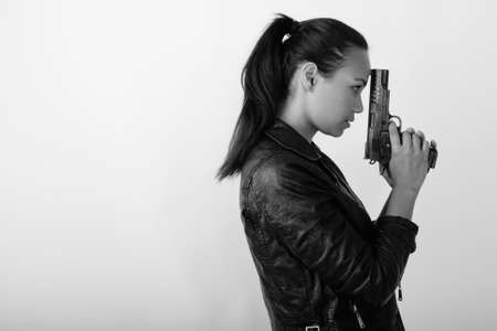Profile view of young Asian woman holding handgun against white backgroundの写真素材