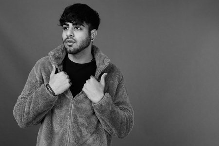 Young handsome bearded Indian man against gray background
