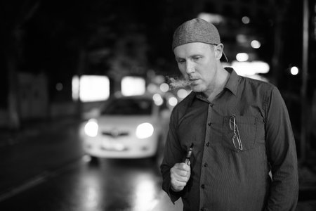 Mature man smoking electronic cigarette in the streets at night