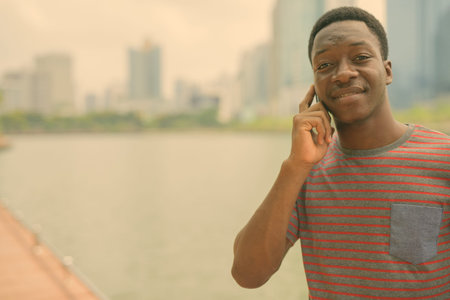 Happy young handsome African man talking on the phone at the park